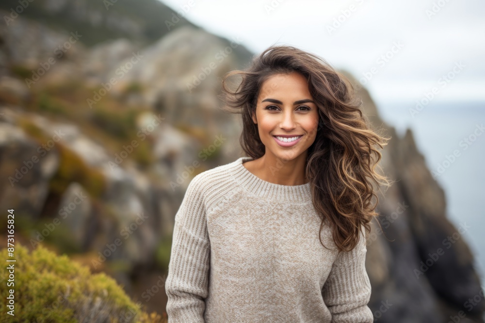 Wall mural Portrait of a happy indian woman in her 20s wearing a cozy sweater isolated on rocky cliff background