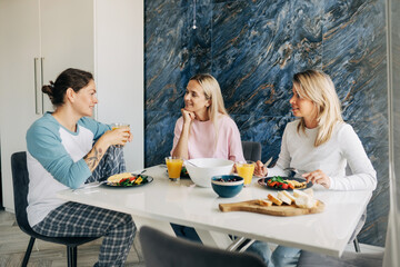 Three women chatting and having dinner at home. Friends met, smiling and relaxing while talking.