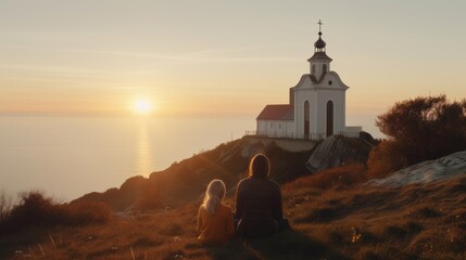 Fototapeta premium A pair of individuals admiring the picturesque view of a church atop a hill during sunset, with the stunning natural landscape, city skyline, and colorful sky as the backdrop