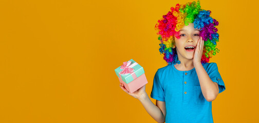 Smiling little boy in clown wig holds gifts in hands. Little boy hold big present box receive gift. Copy pace
