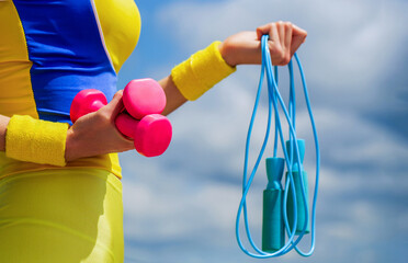 Girl perfect waist with a jump rope in hand, dumbell. Attractive young fitness woman holding dumbell. Slim body, jump rope