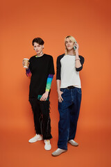 Two young friends wearing colorful outfits pose against an orange background.