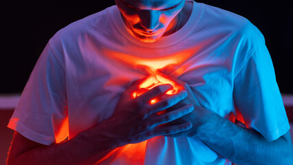 Conceptual photography. The man covers the bright red light coming from his chest with his hands. Mental pain or a broken heart