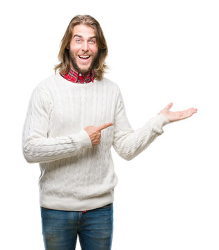 Young handsome man with long hair wearing winter sweater over isolated background amazed and smiling to the camera while presenting with hand and pointing with finger.