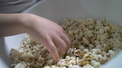 Close-up of a child's hand reaching into a bowl of popcorn, emphasizing the enjoyment and simplicity of a snack time moment