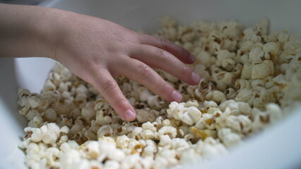 Close-up of a child's hand reaching into a bowl of popcorn, emphasizing the enjoyment and simplicity of a snack time moment