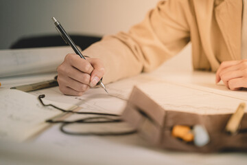 In her architecture office, the woman architect meticulously works on a design drawing by hand,...