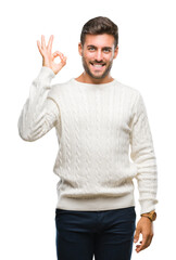 Naklejka premium Young handsome man wearing winter sweater over isolated background smiling positive doing ok sign with hand and fingers. Successful expression.
