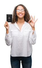 Young hispanic woman holding passport of United States of America doing ok sign with fingers, excellent symbol