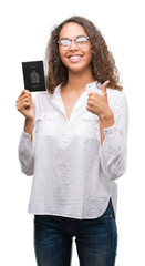 Fototapeta premium Young hispanic woman holding passport of Canada happy with big smile doing ok sign, thumb up with fingers, excellent sign