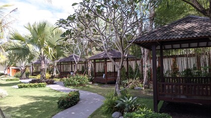 A path leads through a tropical garden with four wooden gazebos. 
