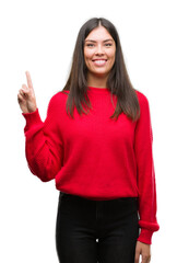 Young beautiful hispanic wearing red sweater showing and pointing up with finger number one while smiling confident and happy.