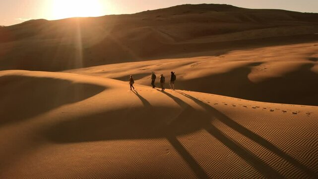 Group of active tourists or hikers walks in sunset desert dunes with long shadows