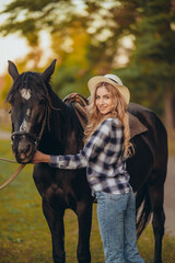 A young woman with a horse stands near a fence in autumn at sunset. Breeding thoroughbred horses...