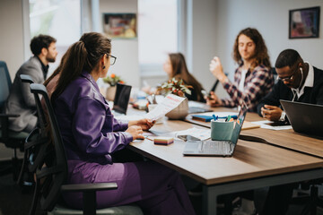 Multiracial business team collaborating and brainstorming together in a dynamic office environment. They are discussing projects with laptops and paperwork on the table.