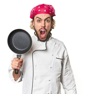 Young Caucasian male chef with frying pan screaming very angry and aggressive.