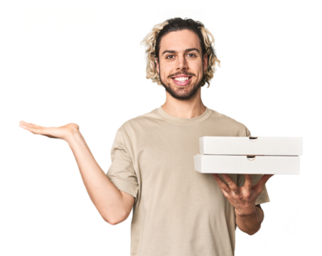 Young man holds pizza boxes for delivery showing a copy space on a palm and holding another hand on waist.