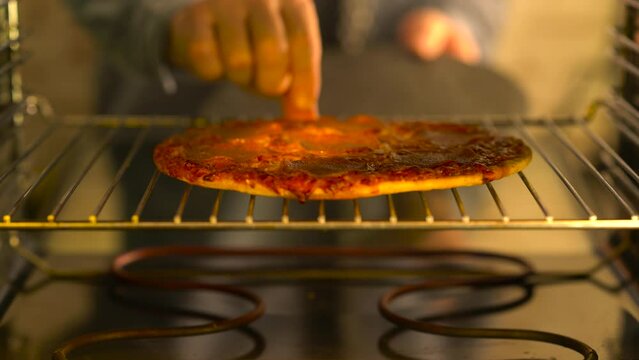 A man opens the oven and takes out a pizza.

