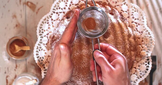 The cook sifts the cinnamon powder over the finished pie.
