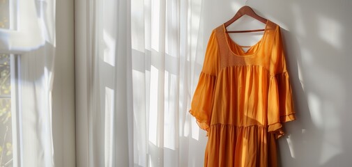 Orange dress hanging in a window with sunlight streaming in.