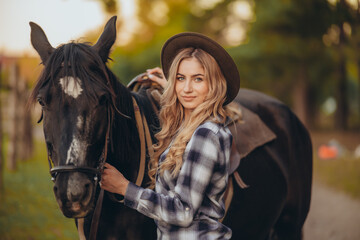A young woman with a horse stands near a fence in autumn at sunset. Breeding thoroughbred horses...