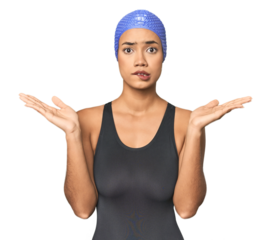Pro Latina swimmer in studio gear confused and doubtful shrugging shoulders to hold a copy space.