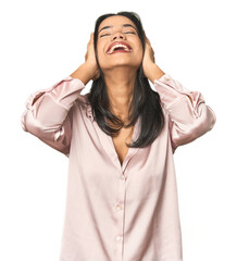 Simple portrait of a young Latina laughs joyfully keeping hands on head. Happiness concept.