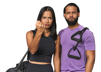 Young Latino couple ready for gym training showing fist to camera, aggressive facial expression.