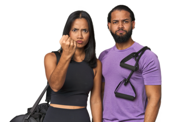 Young Latino couple ready for gym training showing fist to camera, aggressive facial expression.