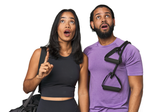 Young Latino couple ready for gym training pointing upside with opened mouth.