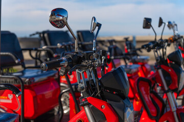 Fototapeta premium Close-up of red three-wheeled electric scooters on a blue sky background on a sunny day. Rent electric tricycle scooters.