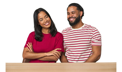 Seated young Latino couple at table smiling confident with crossed arms.