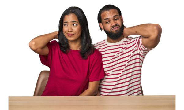 Seated young Latino couple at table touching back of head, thinking and making a choice.