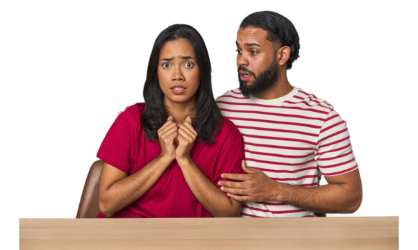 Seated young Latino couple at table scared and afraid.