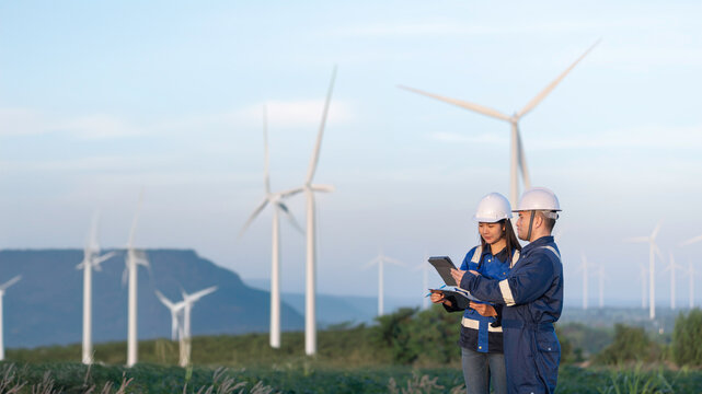 Two engineers working and holding the report at wind turbine farm Power Generator Station on mountain,Thailand people,Technician man and woman discuss about work