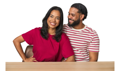 Seated young Latino couple at table confident keeping hands on hips.