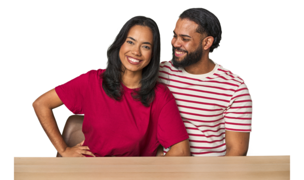 Seated young Latino couple at table confident keeping hands on hips.