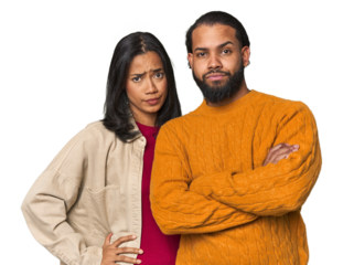 Young Latino couple in studio suspicious, uncertain, examining you.