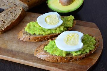 an avocado toast with egg on the wooden cutting board 