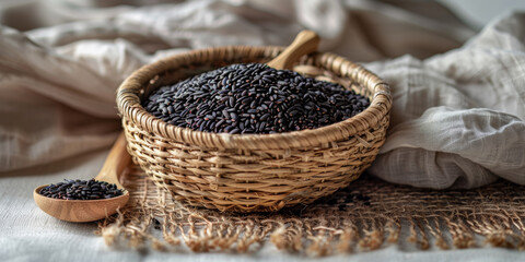 Obraz premium Basket of Black Rice with Wooden Spoon on Rustic Fabric