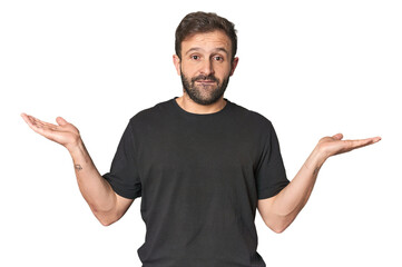 Studio portrait of young Hispanic male confused and doubtful shrugging shoulders to hold a copy space.