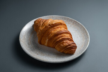 Closeup on french croissant on ceramic plate on grey background