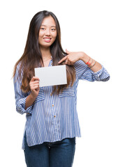 Young asian woman holding blank card over isolated background with surprise face pointing finger to himself