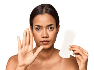 Filipino woman with sanitary pad in studio standing with outstretched hand showing stop sign, preventing you. © Asier