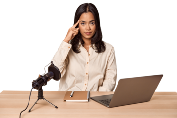 Woman records podcast with laptop pointing temple with finger, thinking, focused on a task.