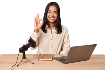 Woman records podcast with laptop cheerful and confident showing ok gesture.