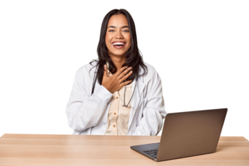 Young Filipino doctor with laptop in studio laughs out loudly keeping hand on chest.