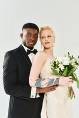A beautiful blonde bride in a wedding dress and an African American groom in a tuxedo holding a...