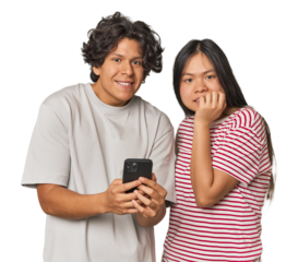 Young interracial couple using smartphone biting fingernails, nervous and very anxious.