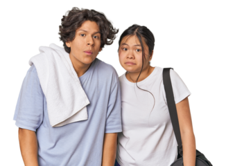 Young interracial athletic couple in studio shrugs shoulders and open eyes confused.